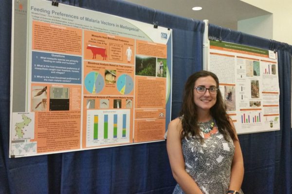 Student poses with research poster.
