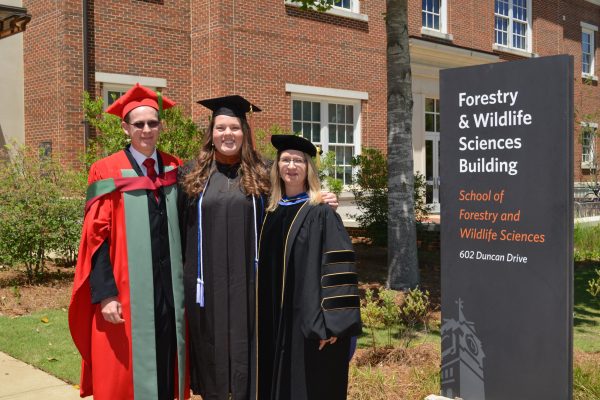 student and faculty pose together outside sfws building after graduation