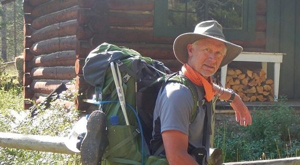 interpretive park ranger Orville "Butch" Bach stands outside log cabin