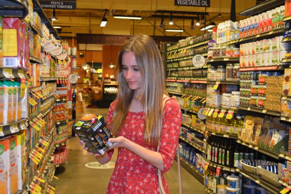 A woman stands in a grocery aisle examining a product's packaging.