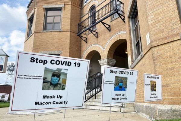 "Stop COVID-19, Mask Up Macon County" yard signs pictures in front of a building.