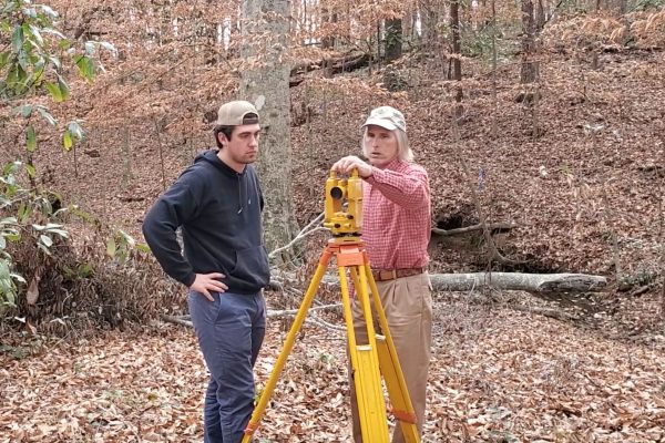 Dr. Tom Gallagher assists a student with a surveying tool.