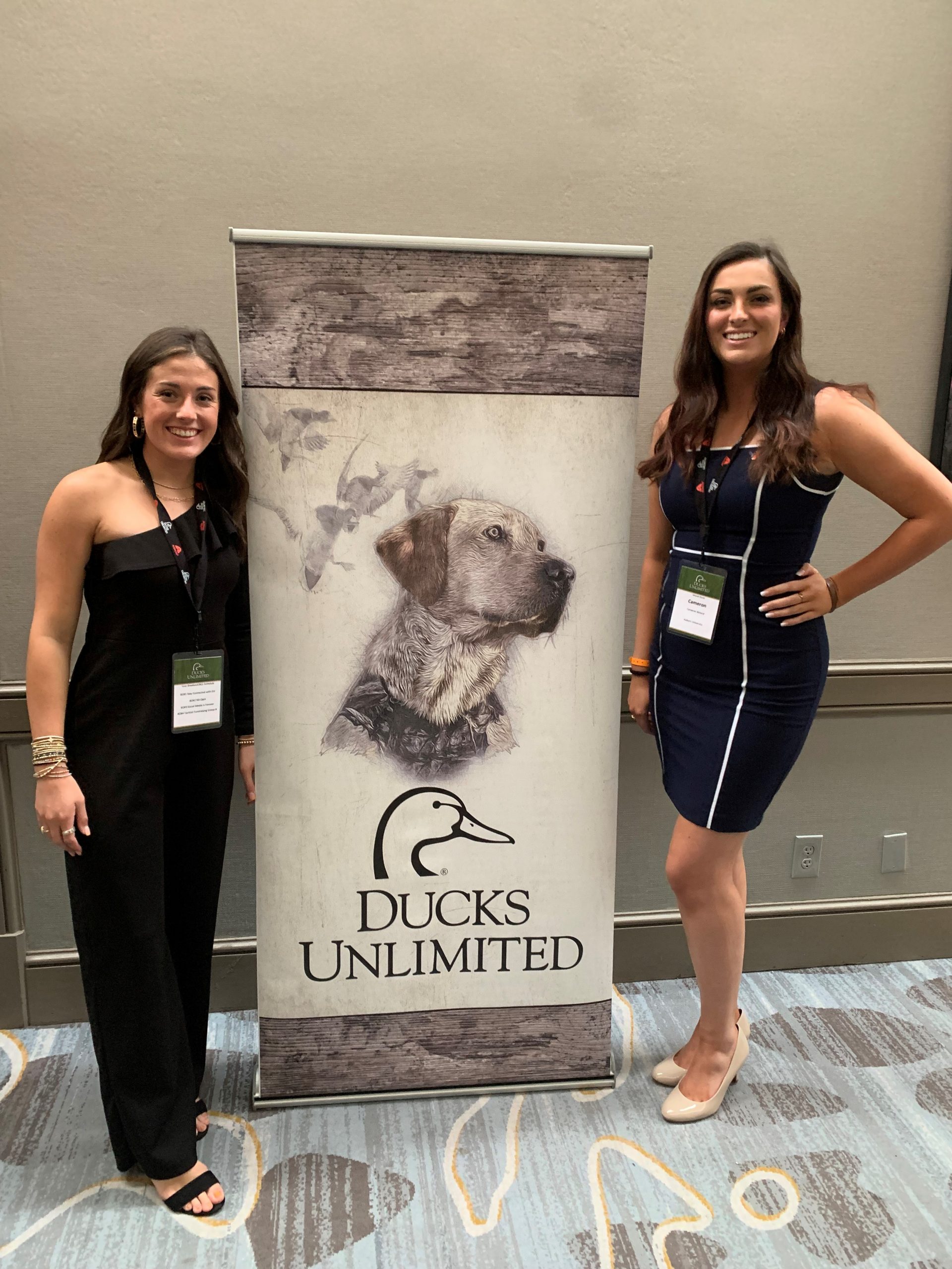 Medlin and Boland dressed in business casual stand on each side of a Ducks Unlimited banner.