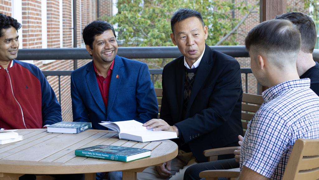 Daowei Zhang seated at table looking at books with graduate students