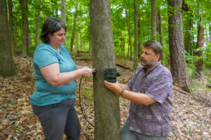 Jean Fantle-Lepczyk (left) and Chris Lepczyk (right) mount a game camera to a tree.