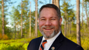 Man in suit smiling in the woods.