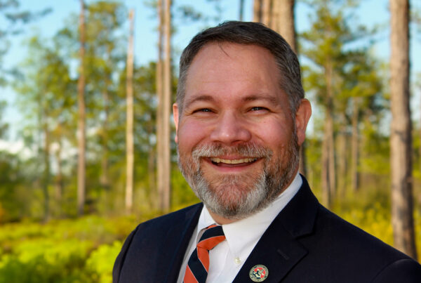 Man in suit smiling in the woods.