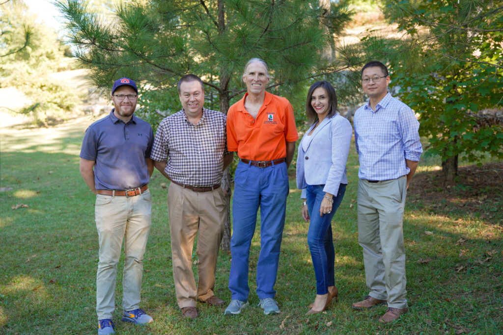 A group of five people pose for a photo while standing in grass.