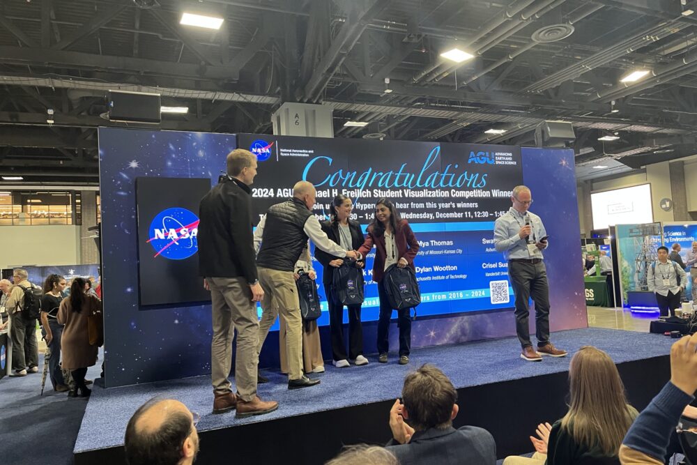 Woman shaking hands with man on stage after winning a prize.