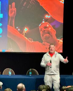 Man presenting on a stage to a crowd of people