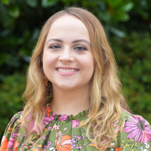Kelsey Shoemaker smiles for a headshot photo with a green background.