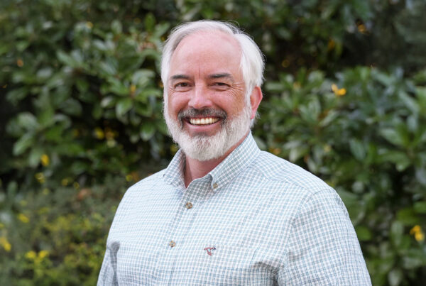 Jim Noles stands in front a green background for a headshot photo.