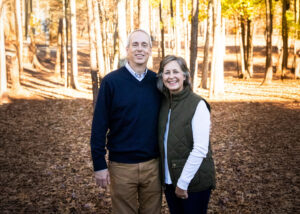 Jim and Janice Kelly pose for a photo in a forested fall landscape.