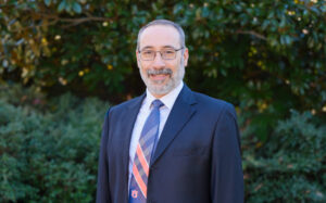 Latif Kalin poses for a headshot against a lush background.