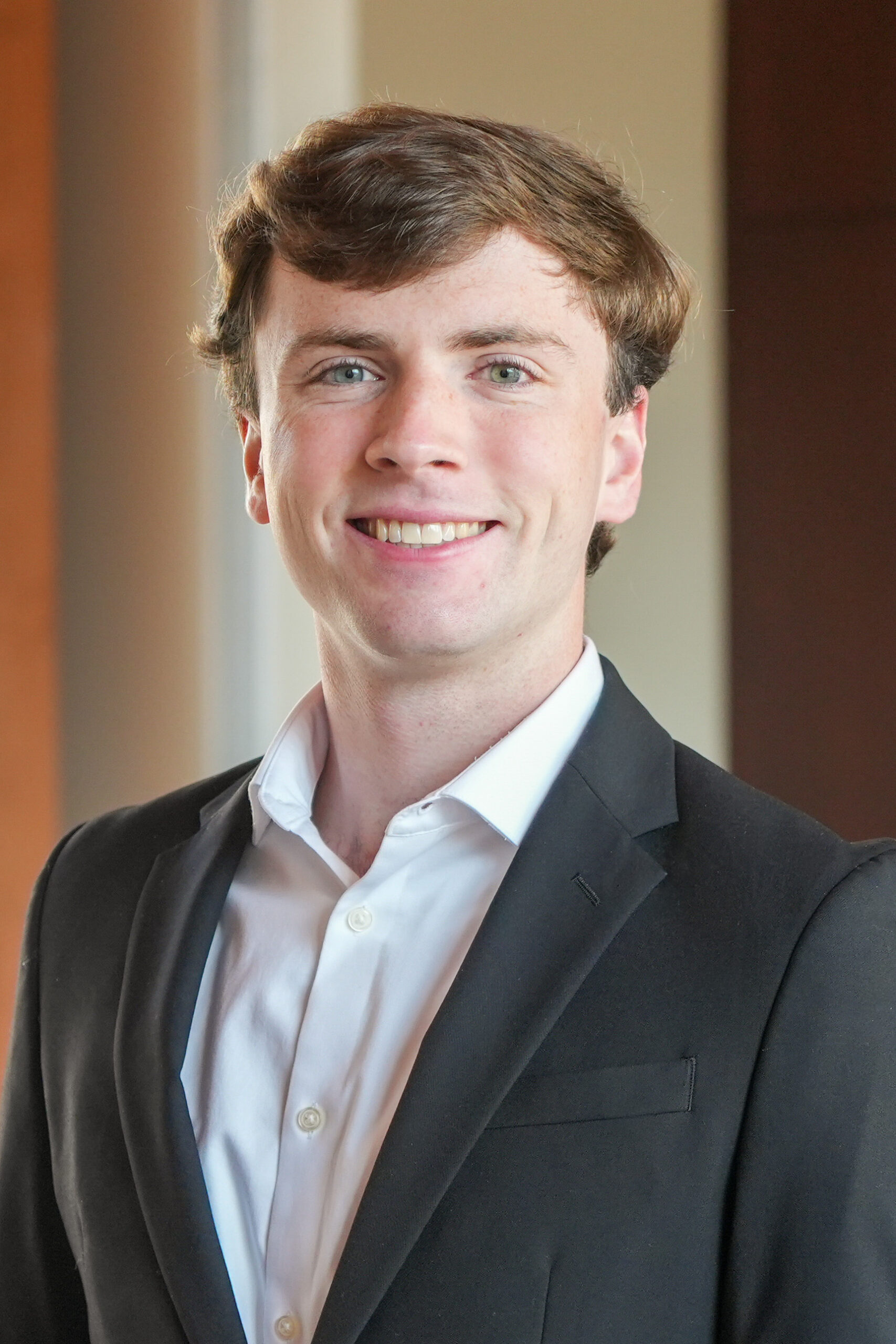 Matt Long standing standing in a dark suit jacket smiling.