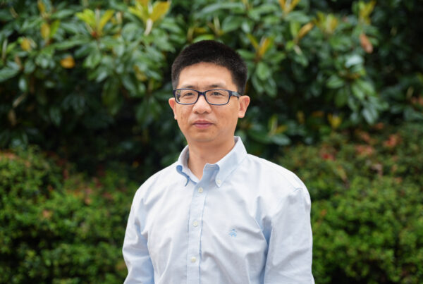 Zutao Ouyang poses for a headshot in front of a lush green backdrop.