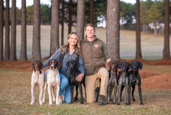 Dylan Thomas and his wife kneel with six bird dogs in a field