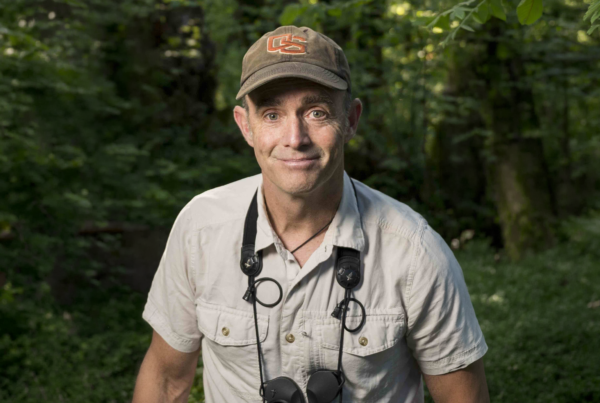Matthew Betts poses for a photo in the woods with binoculars around his neck.