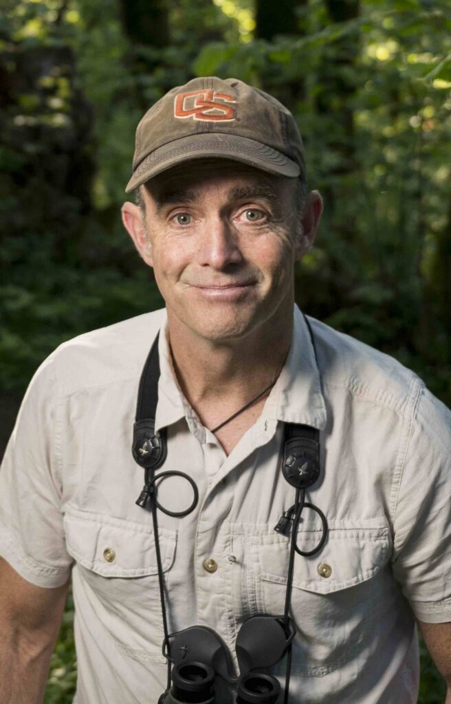 Matthew Betts poses for a portrait outdoors with binoculars hanging from his neck.