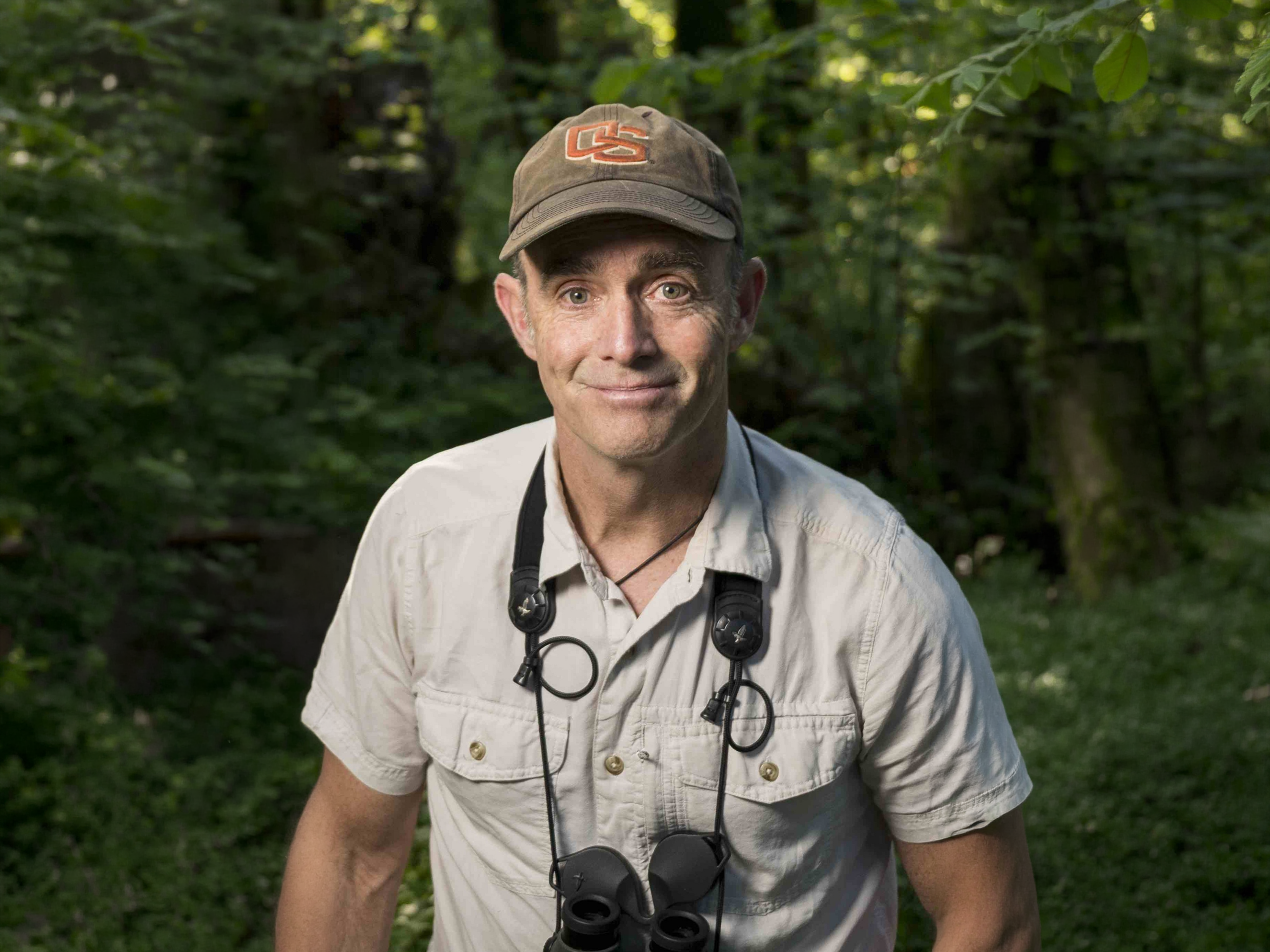 Matthew Betts poses for a photo in the woods with binoculars around his neck.