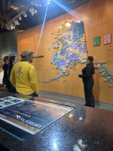 Person presenting a Ranger Talk indoors at the Southeast Alaska Discovery Center, with display exhibits and audience nearby.