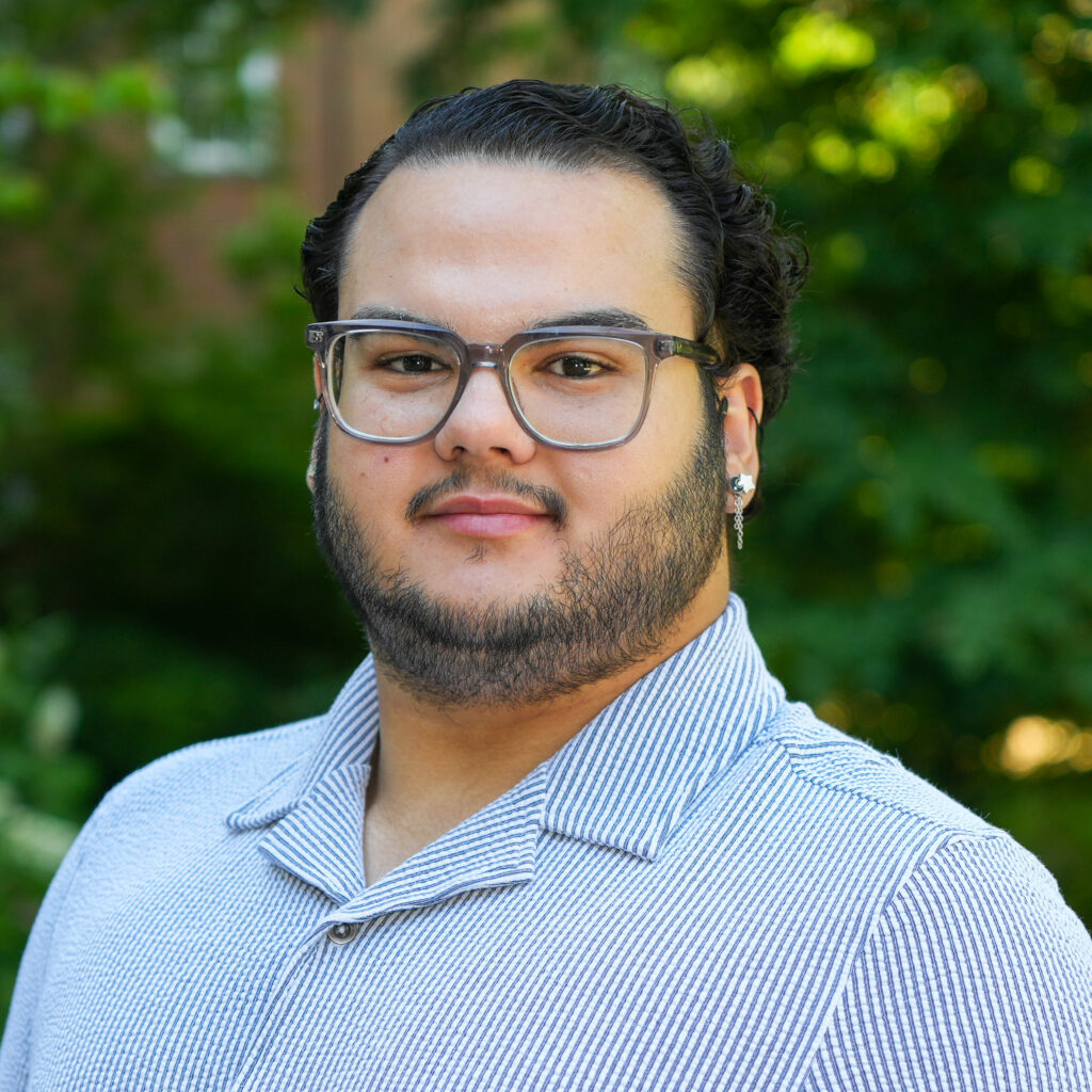 Gabriel Silva poses for a headshot against a forest background