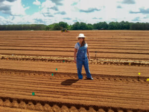 Nina Payne stands in a tree nursery with a tractor operating behind her.