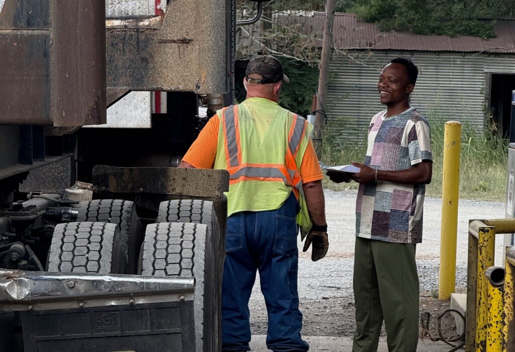 two men talk next to a logging truck at a fuel station