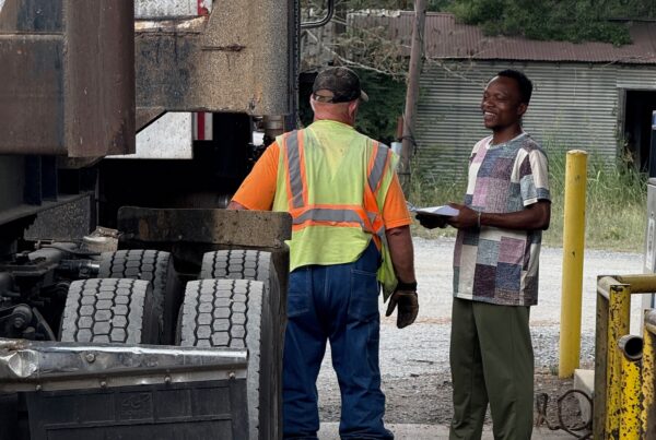 two men talk next to a logging truck at a fuel station