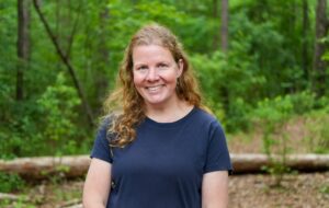 Sarah Crim poses for a headshot against a forested background.