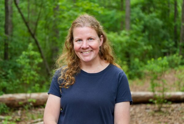 Sarah Crim poses for a headshot against a forested background.