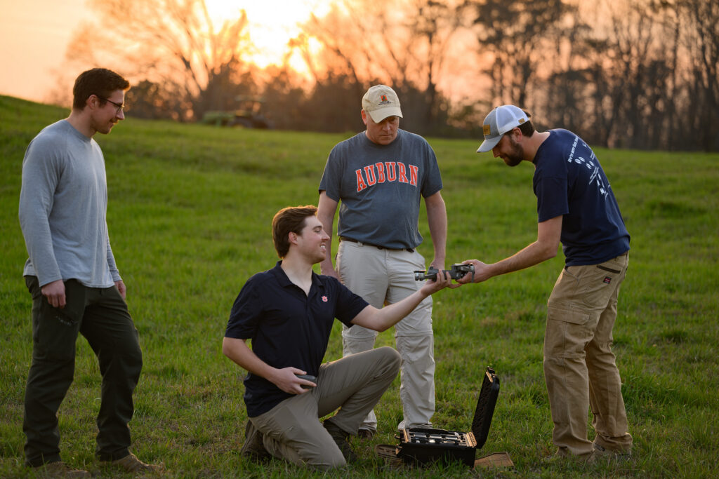 four men handle a drone while standing in a field