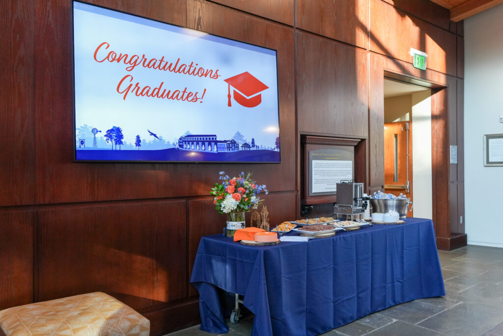 A decorative blue table with a spread of food sits below a monitor that displays "Congratulations Graduates"