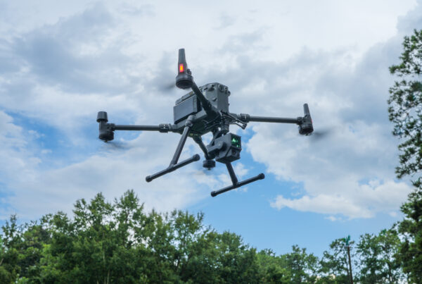 drone flies above a field near a forest