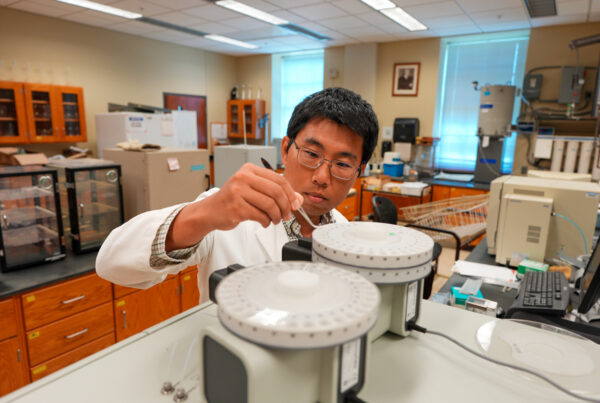 Man shown loading soil samples into an Elemental Analyzer to generate nutrient data for AI-based subsurface biogeochemical modeling.