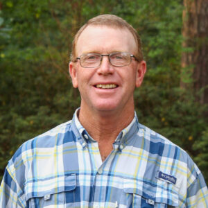 Ken Newby poses for headshot in front of forest background