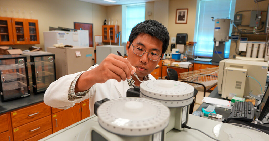 Man shown loading soil samples into an Elemental Analyzer to generate nutrient data for AI-based subsurface biogeochemical modeling.