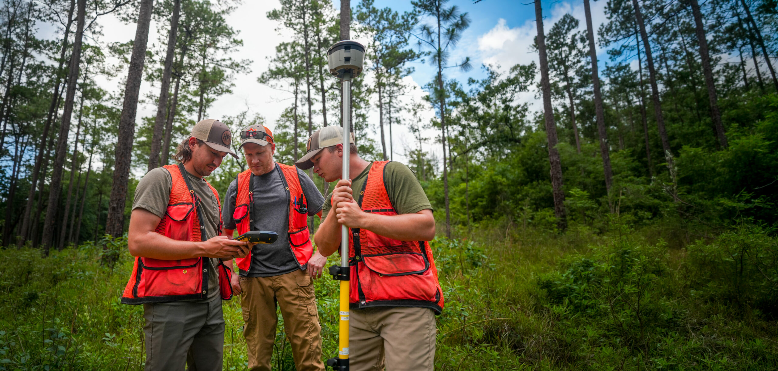 Two forestry students and a professor use technology in the forest.