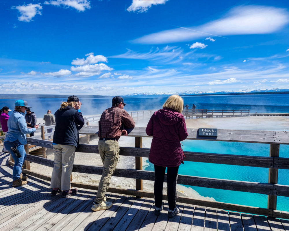 A group of people lean on a rail at a natural spring.