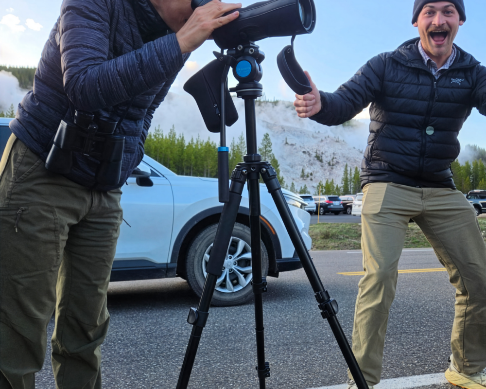 A man poses for a photo with his coworker looking through a lens.
