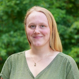 Abigail Meeks poses for a headshots against a lush, green background