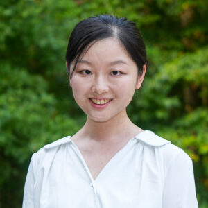Sijin Guo poses for a headshot against a lush, green background